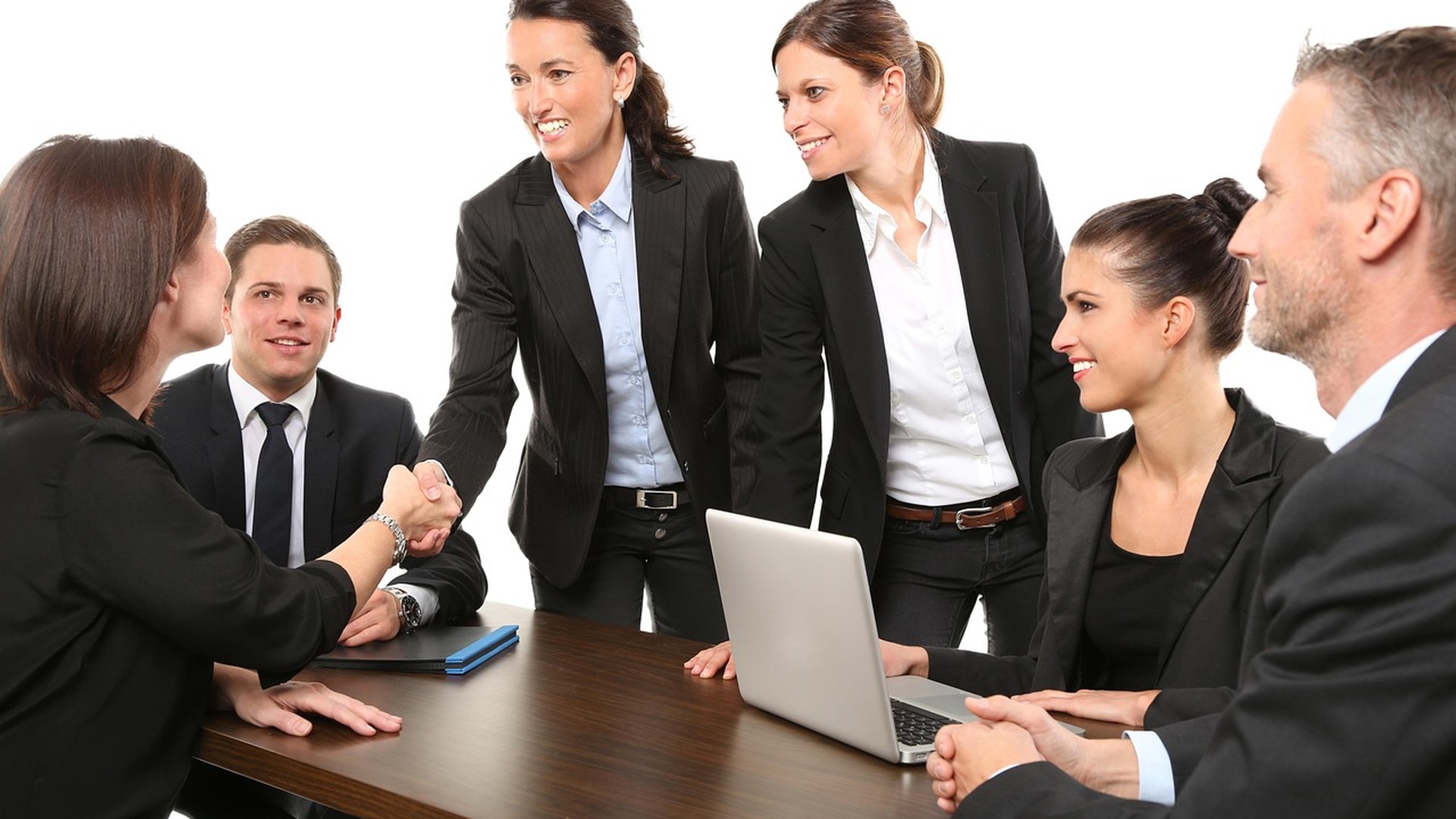 Two business professionals shaking hands over an open laptop