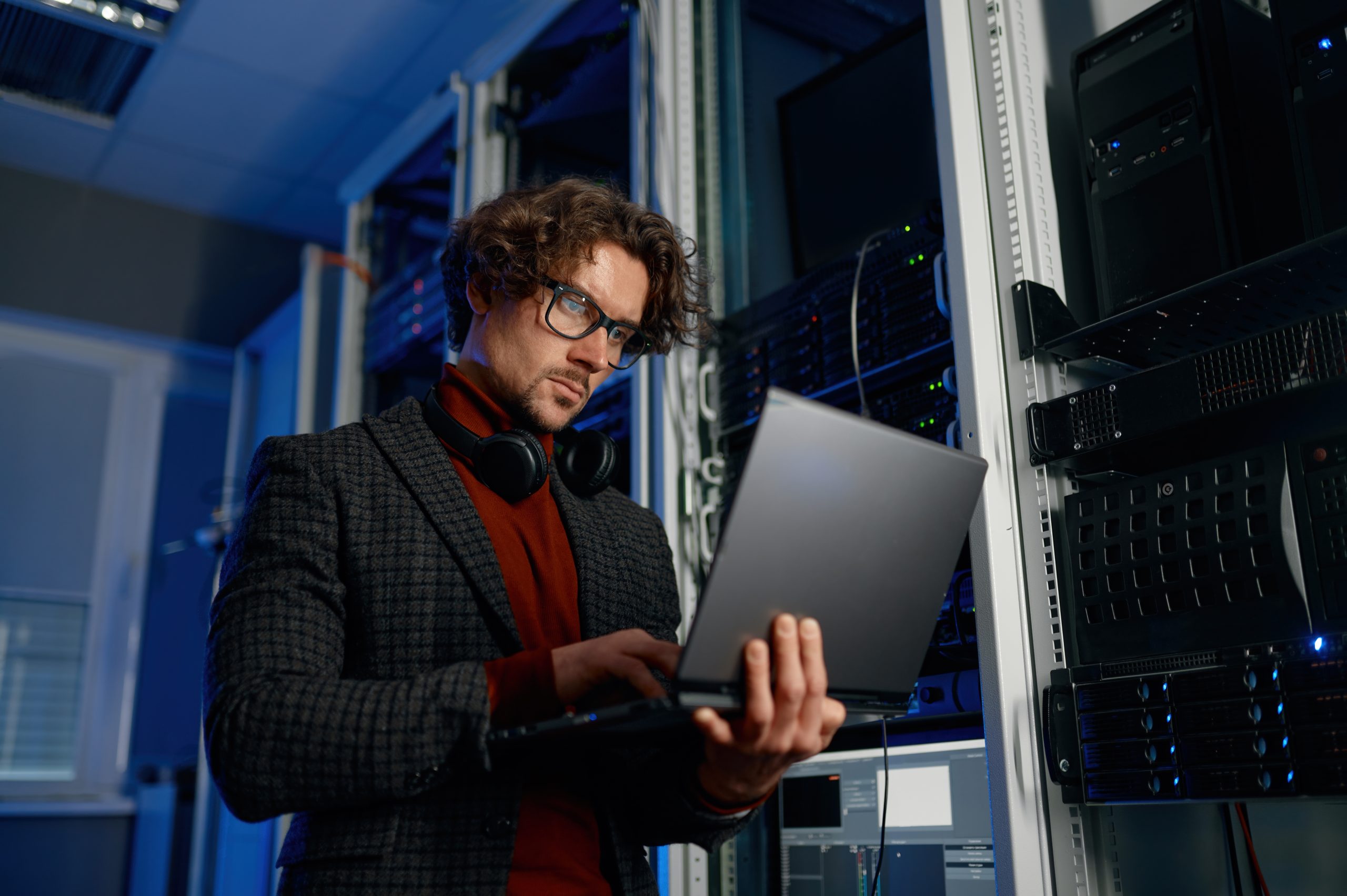 Contact image by O&O Systems IT technician working on a laptop inside a server room with rack equipment