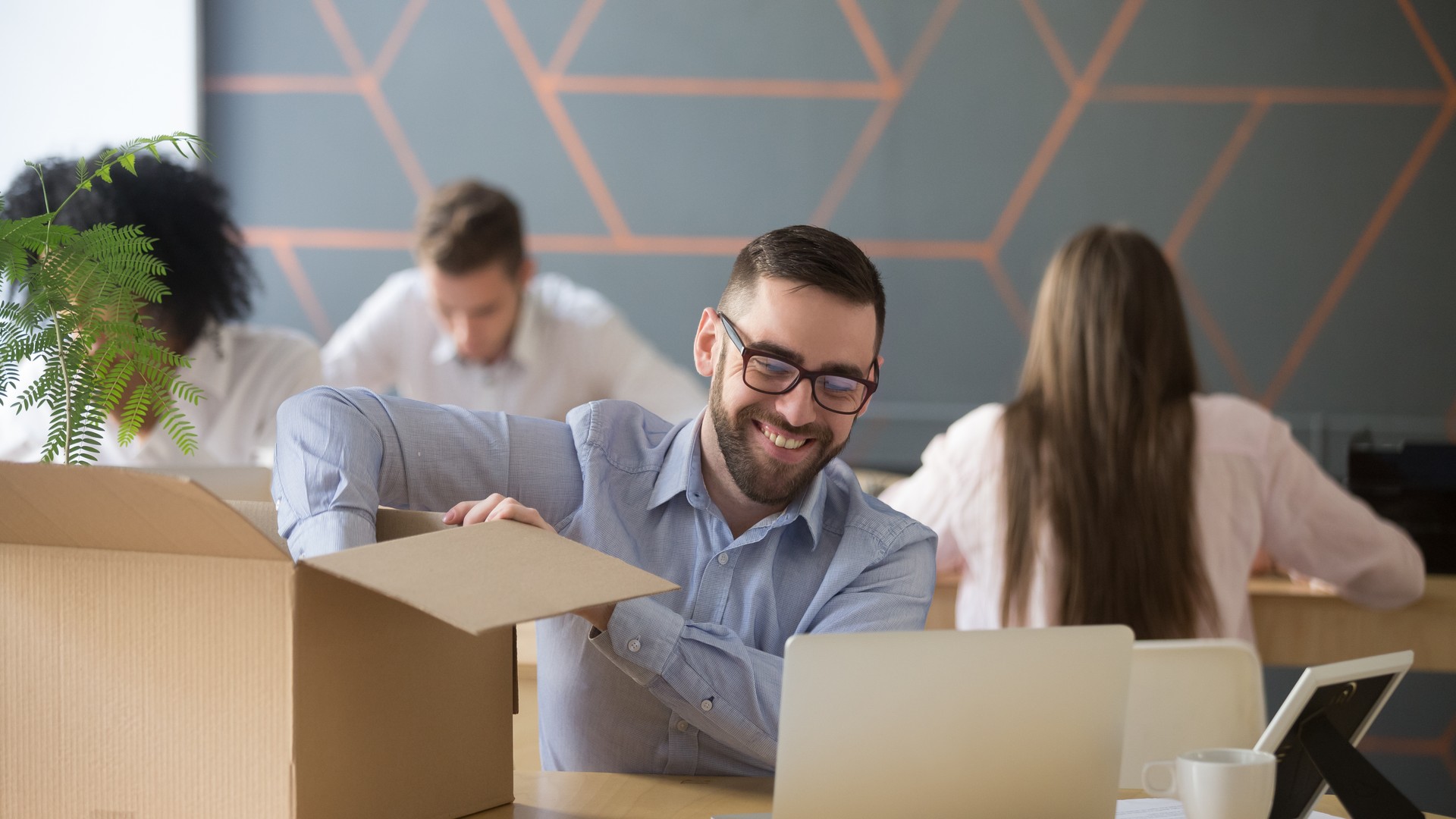 Person opening a cardboard box beside a laptop in a shared office.