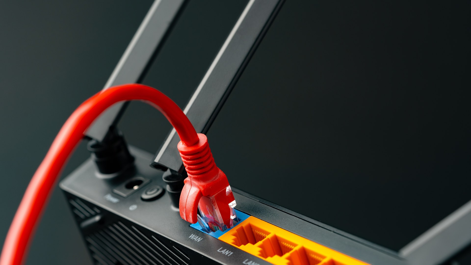 Patch Management image by O&O Systems Red Ethernet cable plugged into a router beside yellow network ports and upright antennas.