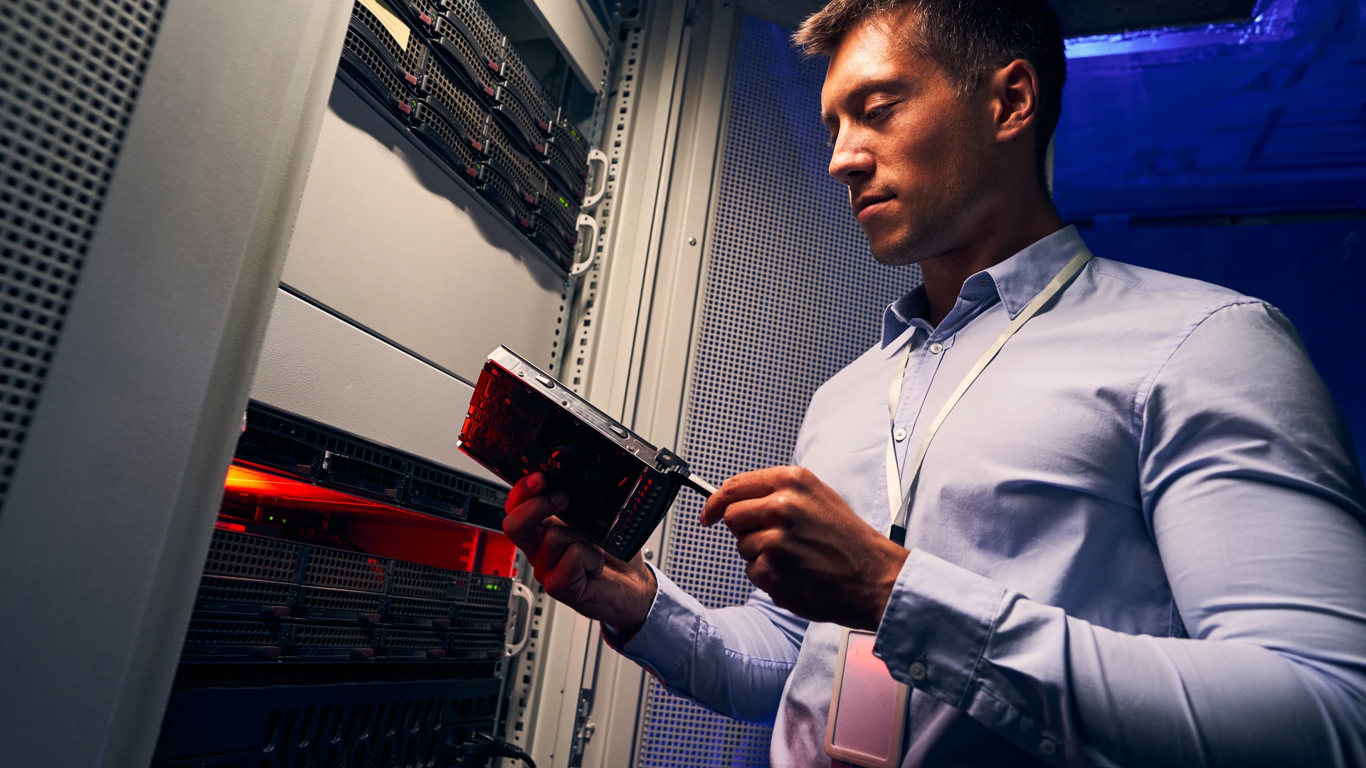 Man holding an electronic component and a screwdriver beside an open server rack.