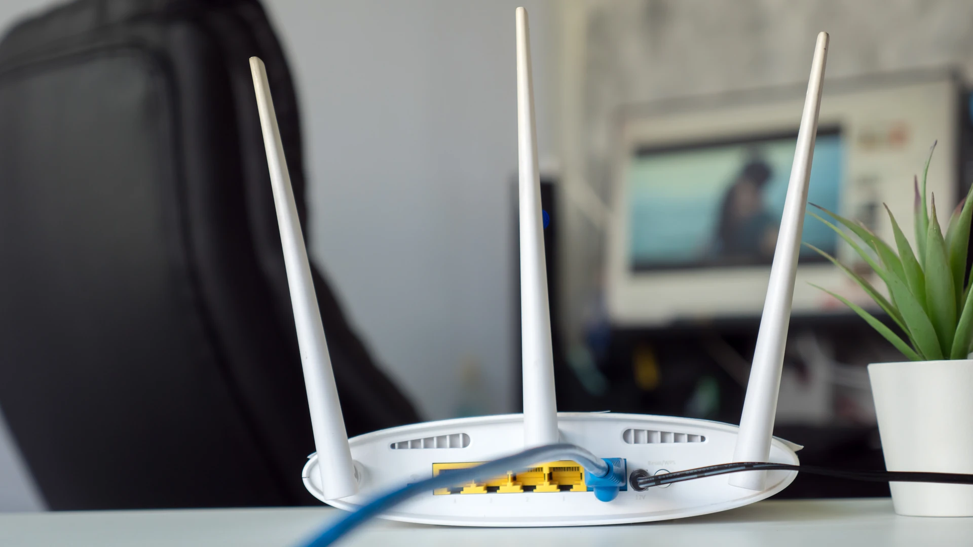 Patch Management image by O&O Systems A white wireless router with three antennas sits on an office desk with a blue network cable plugged into its back