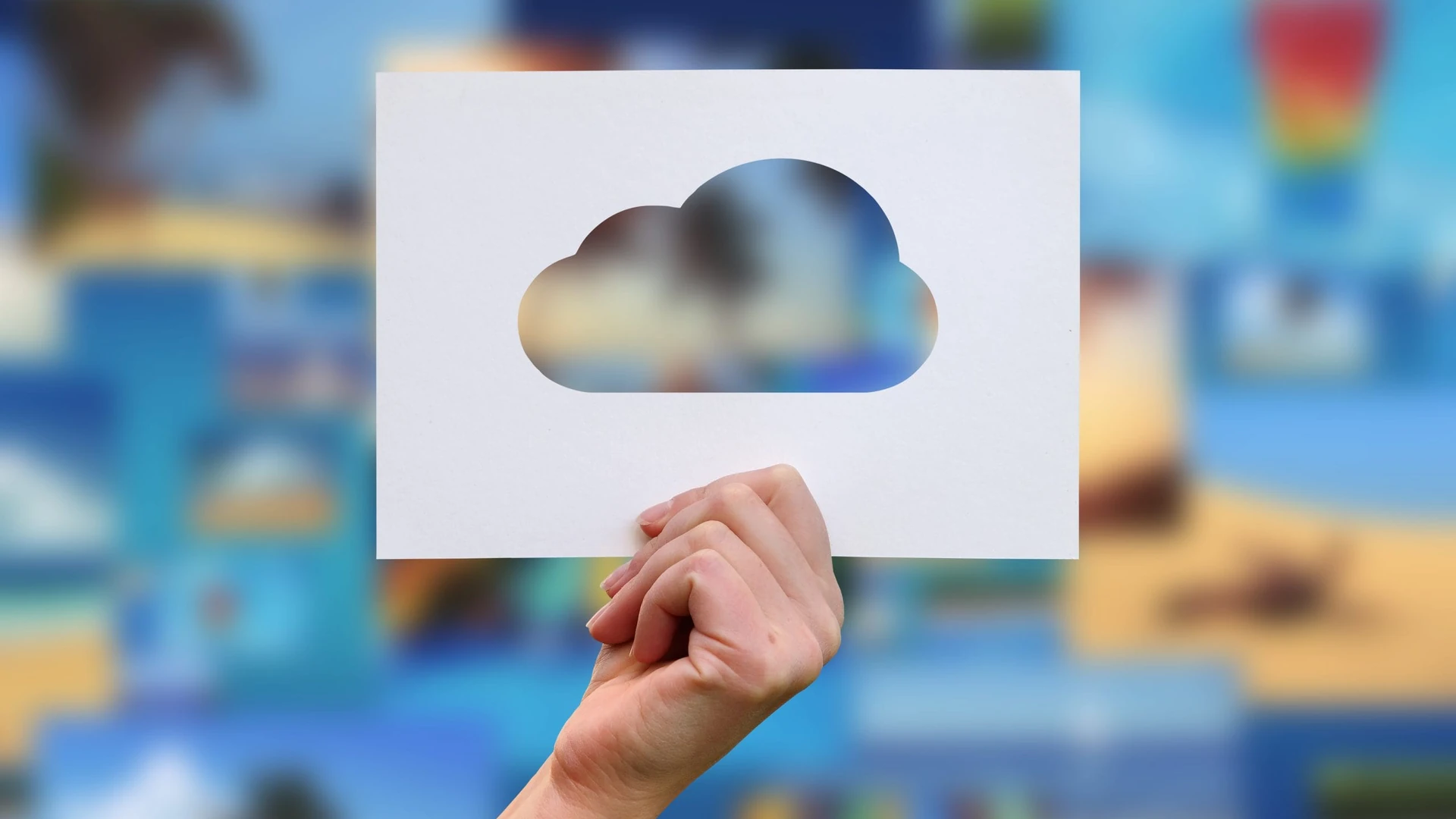 A hand holding a sheet of white paper with a cloud-shaped cutout against a blurred blue background